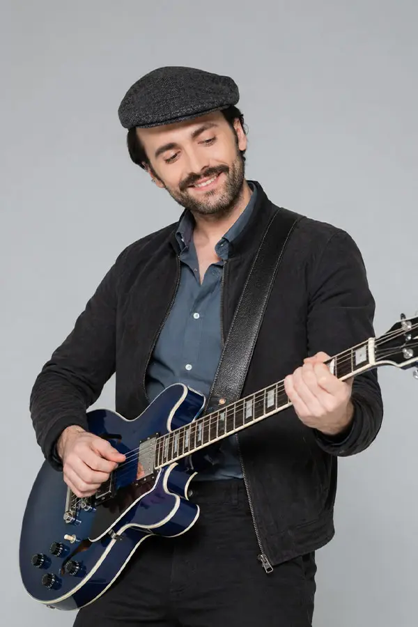 Man in a flat cap playing a blue semi-hollow electric guitar