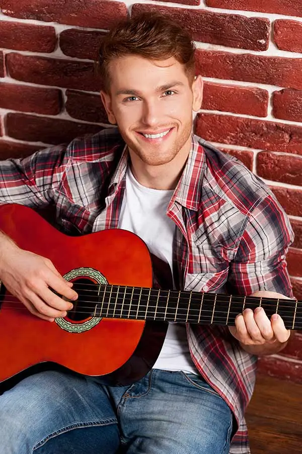 Smiling man playing a classical guitar against a brick wall