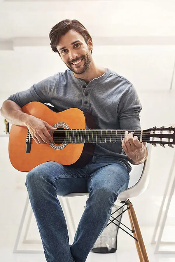 Man seated on a chair playing a classical guitar