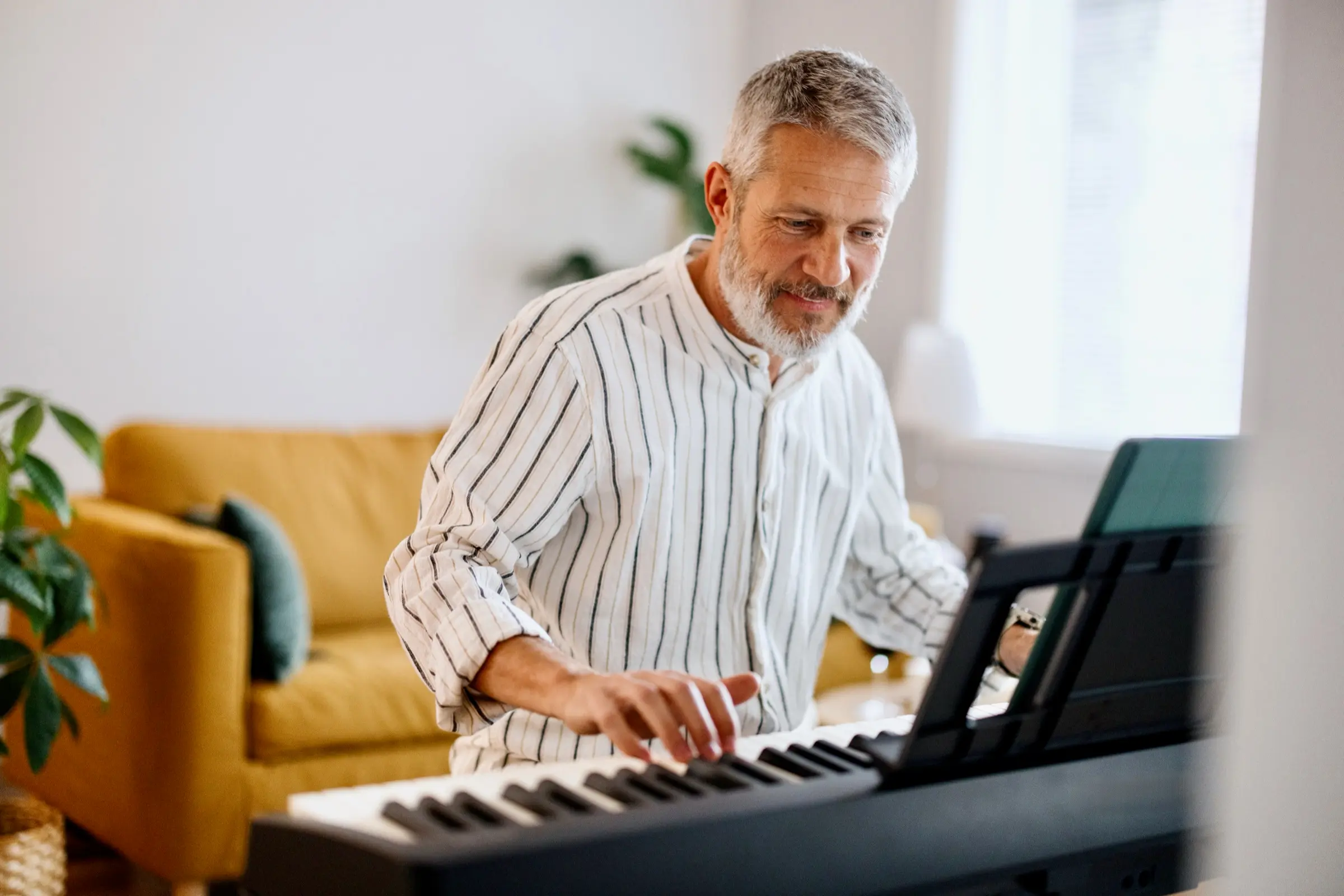 Grey-haired man playing a digital piano in his living room.
