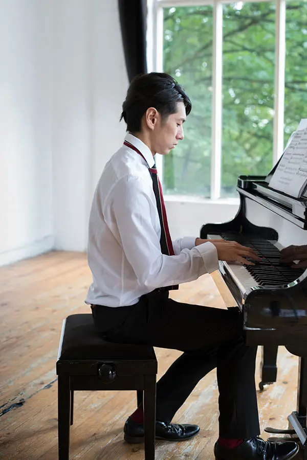 Man playing a grand piano beside a window