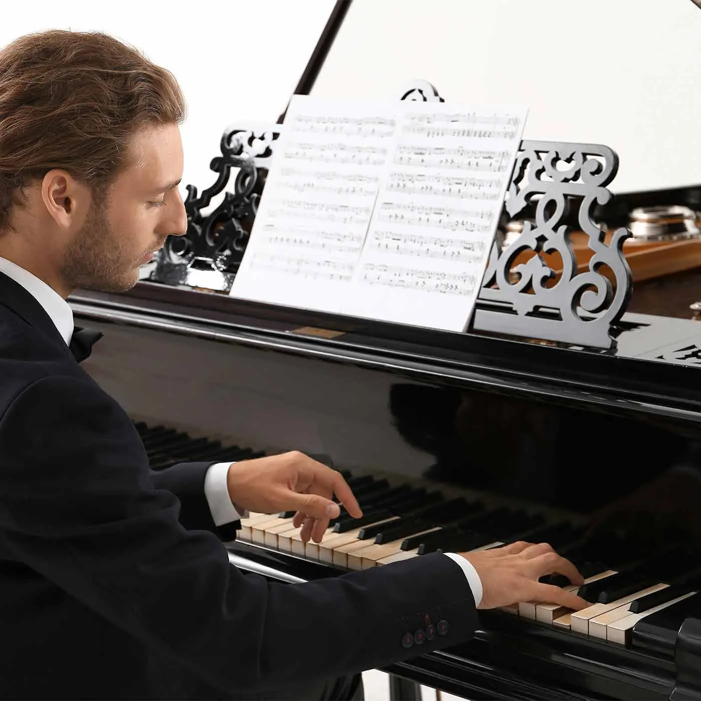 Man in a suit playing a grand piano with sheet music
