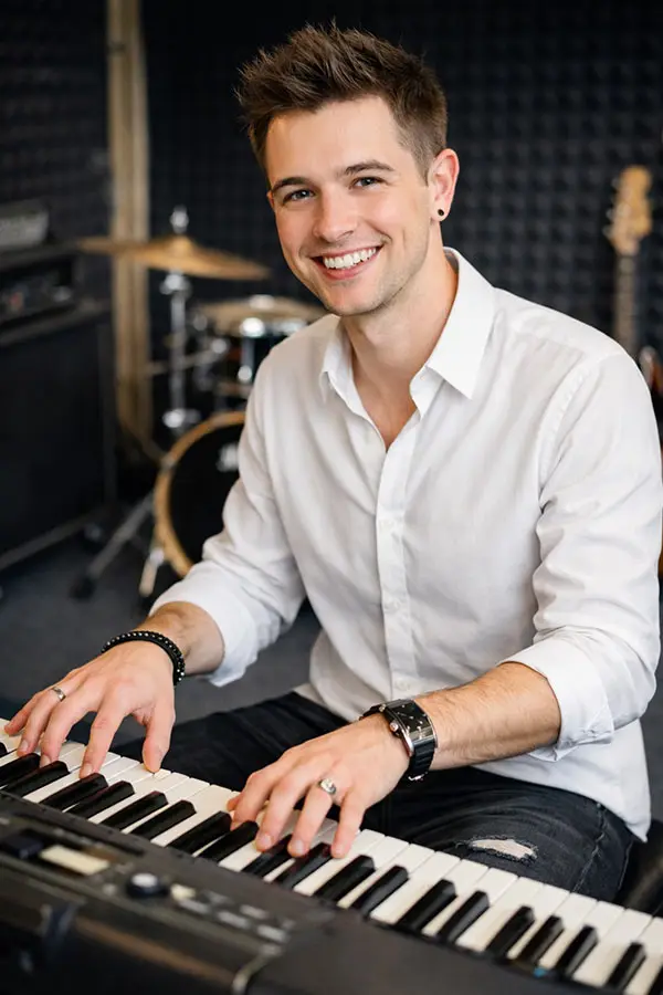 Smiling man playing a keyboard in a music studio