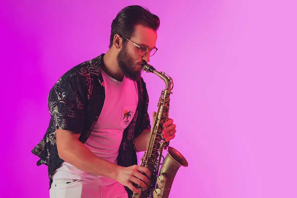 Man in glasses playing saxophone against a pink background