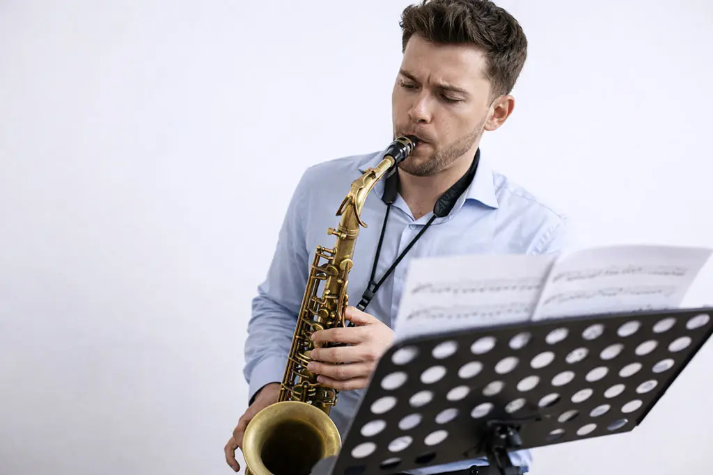 Man in a blue shirt playing saxophone behind a music stand