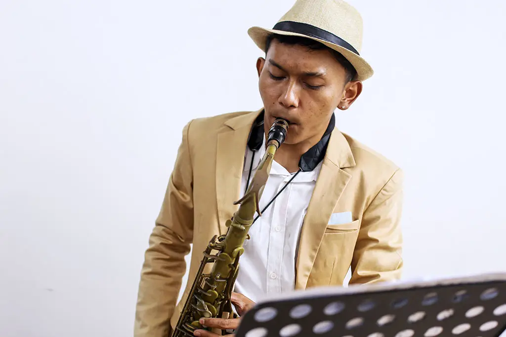 Man in a beige hat playing saxophone beside a music stand