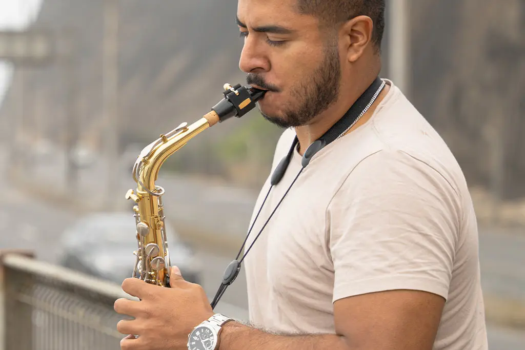 Man playing a saxophone outdoors beside a railing