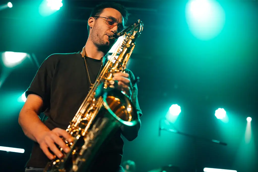 Man in glasses playing saxophone under green stage lights
