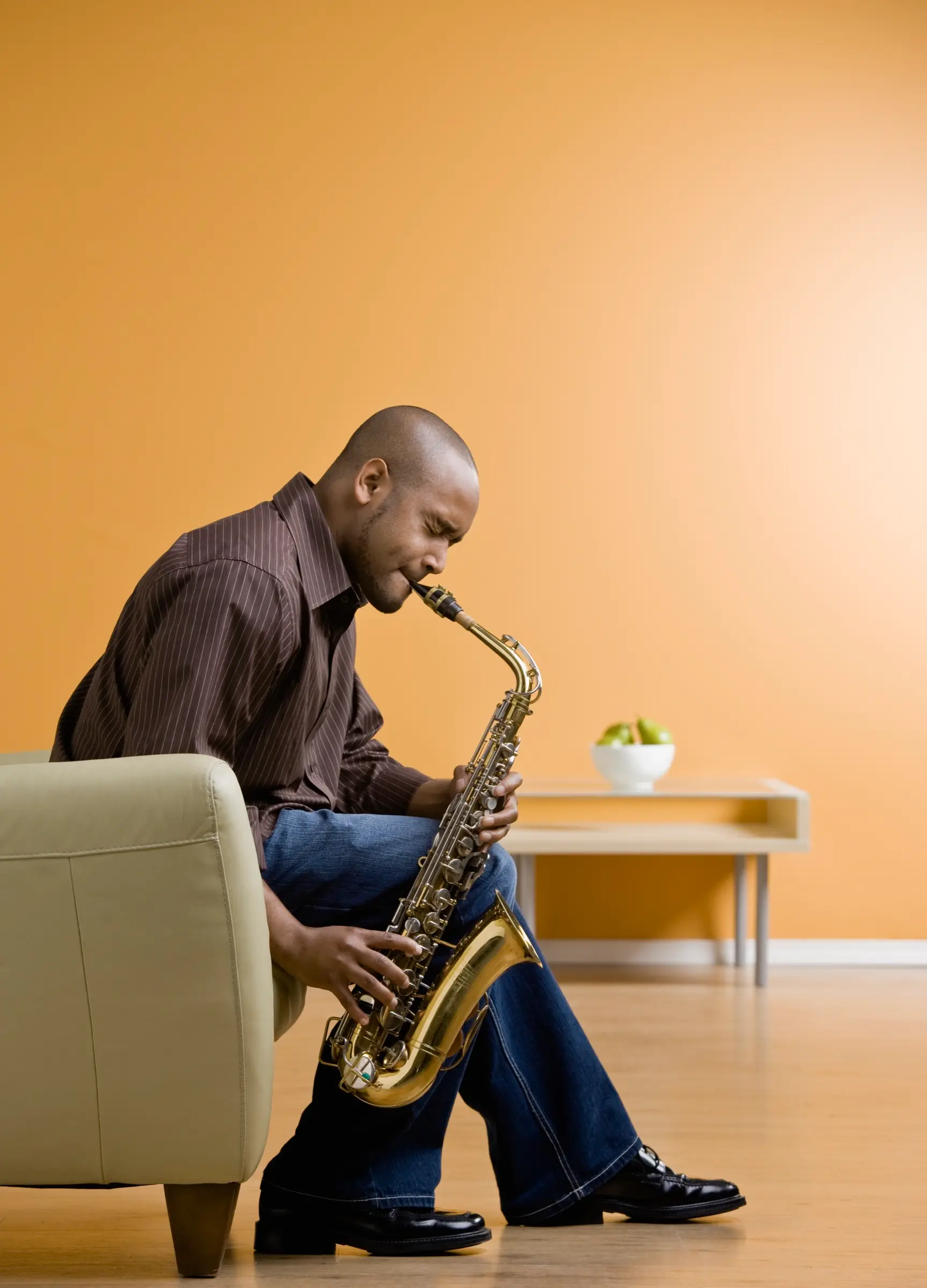 Man sitting in an armchair playing the saxophone.