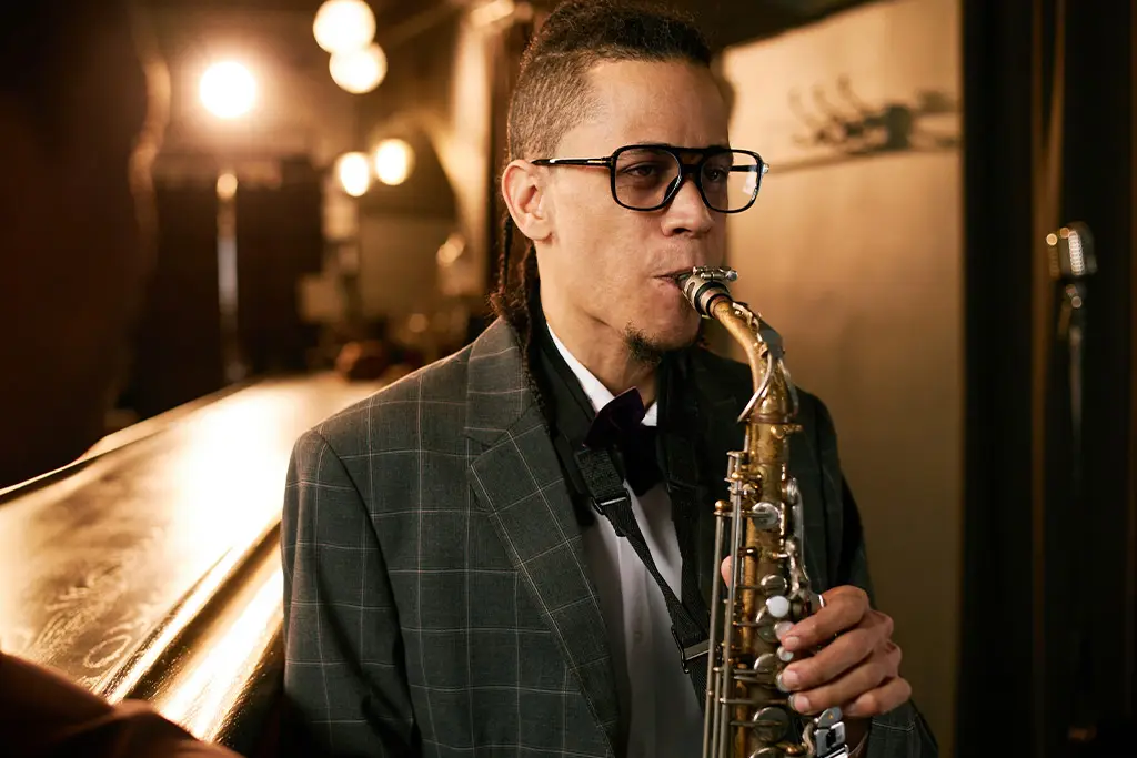 Man with glasses in a checked suit playing saxophone indoors
