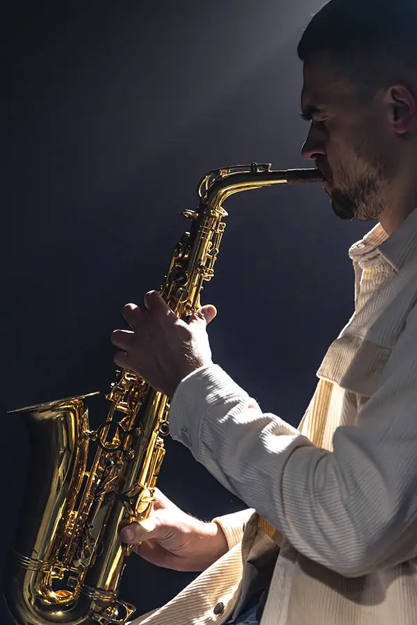 Man in a cream shirt playing saxophone in dramatic side lighting
