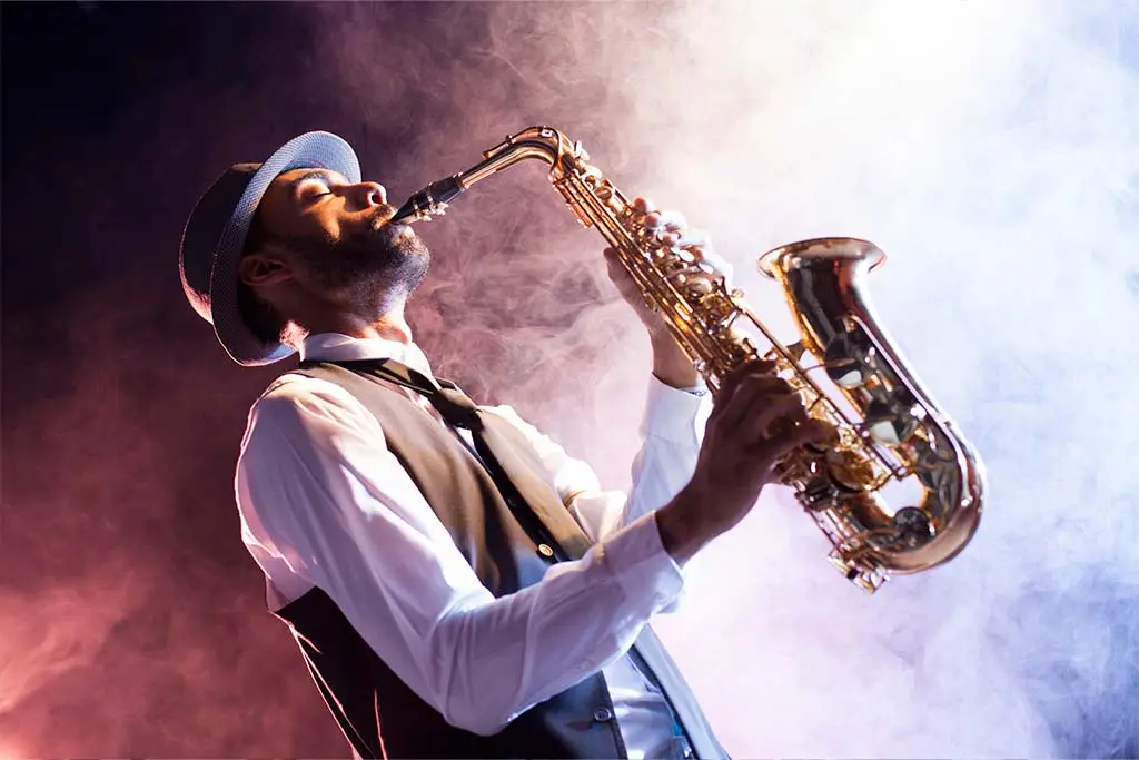 Man in a hat playing saxophone amid coloured smoke