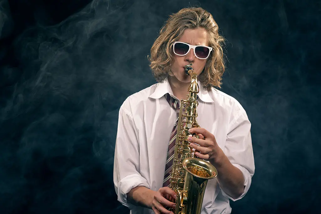 Man wearing sunglasses playing saxophone in smoky lighting