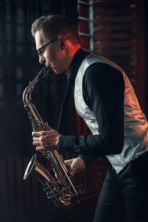 Man with glasses and a waistcoat playing saxophone indoors