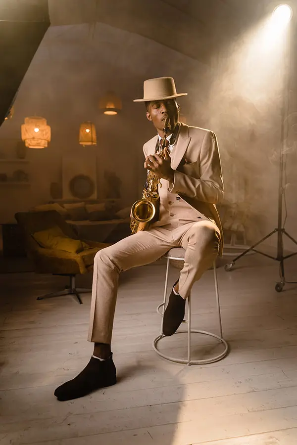 Man in a beige suit and hat playing saxophone on a stool