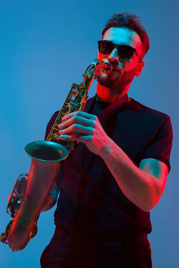 Man in sunglasses playing a saxophone under colourful lighting