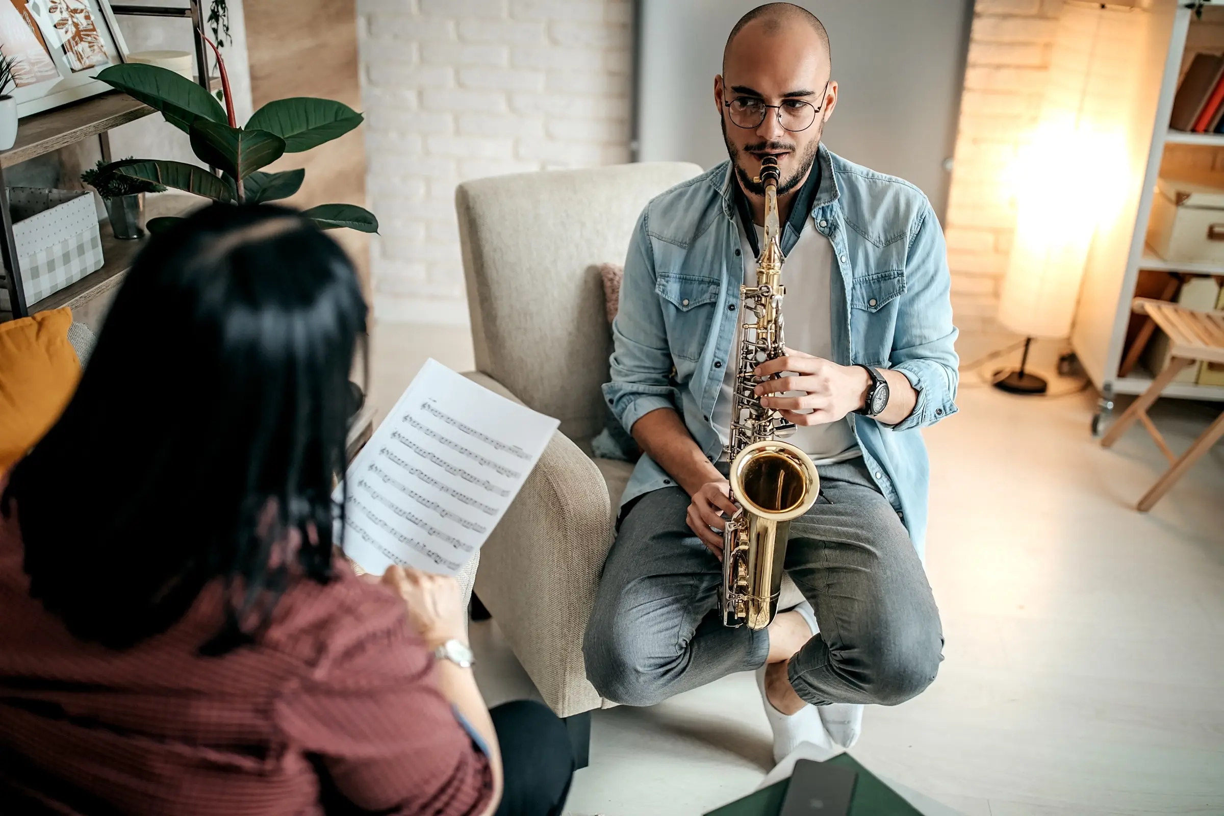 Man playing the saxophone while a woman follows the sheet music.