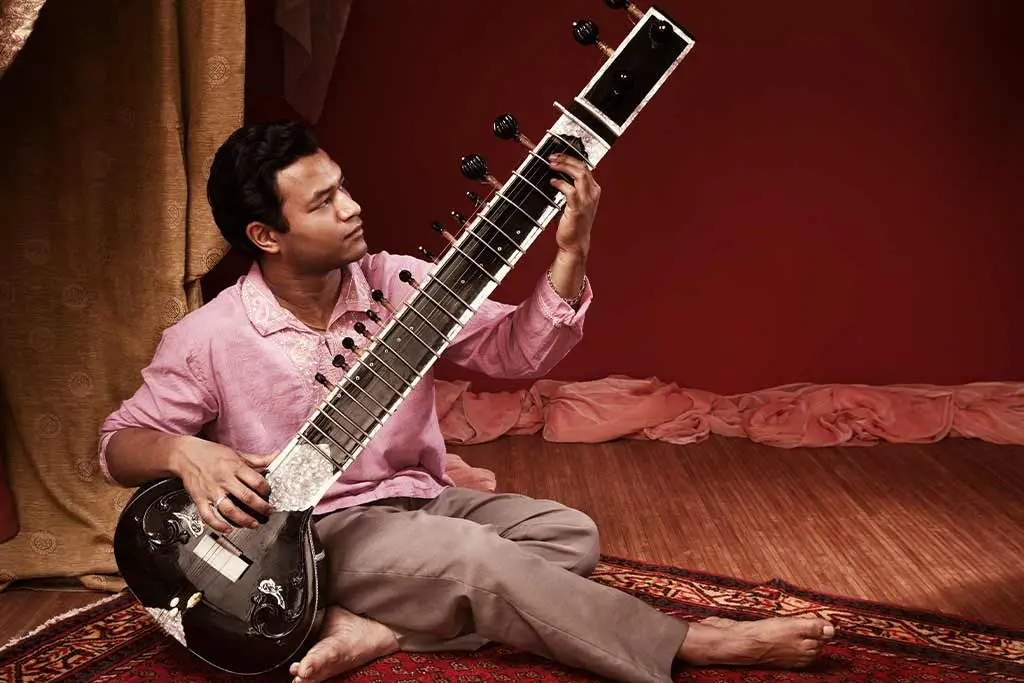 Man sitting on a rug playing a sitar