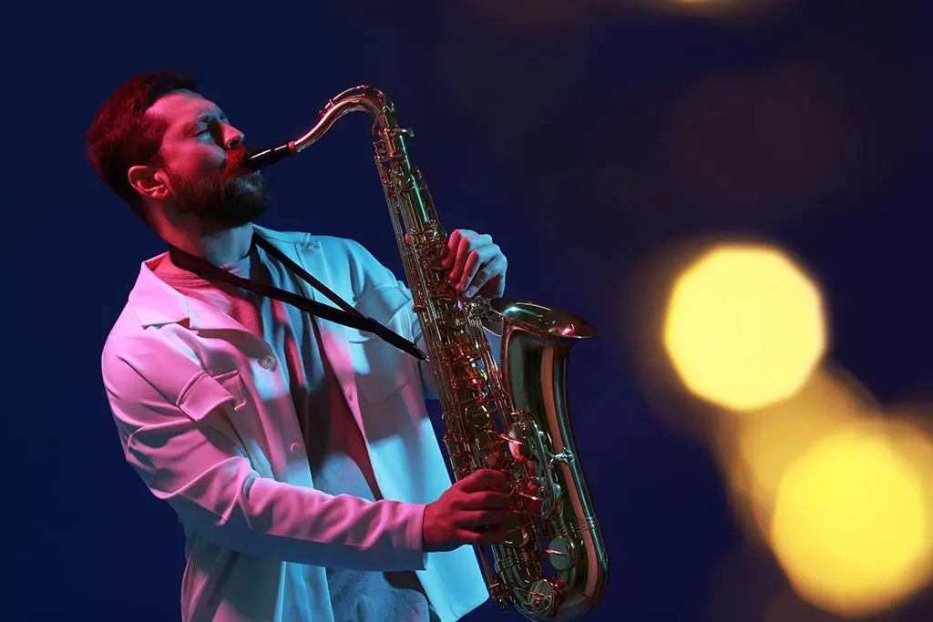 Man in a white jacket playing tenor saxophone with blurred stage lights