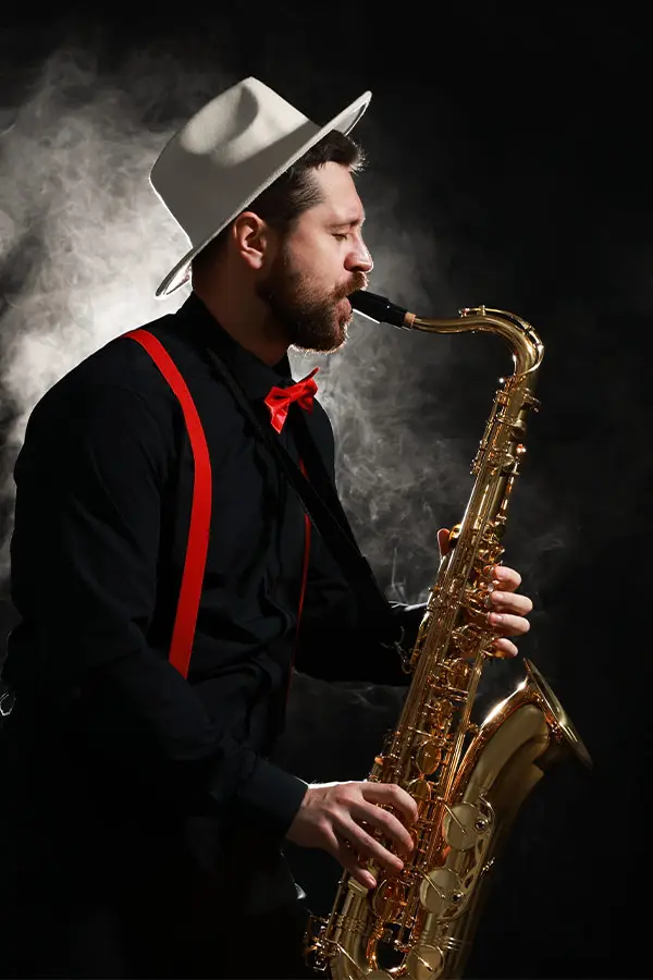 Man in a white hat playing tenor saxophone in smoky light