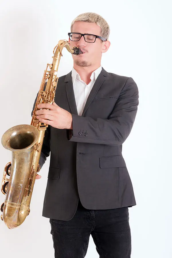 Man with glasses playing tenor saxophone in a suit