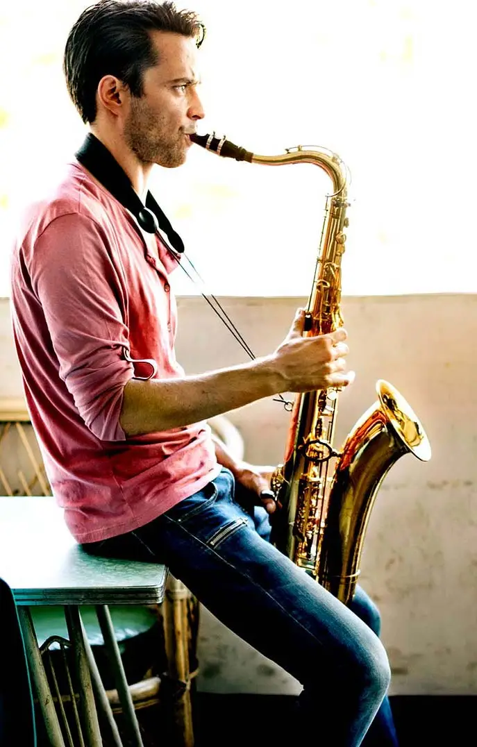 Man in a pink shirt playing tenor saxophone indoors