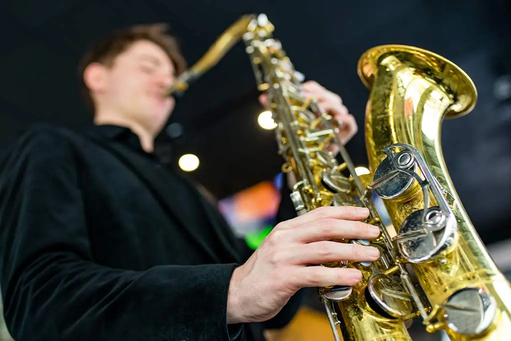 Man in a dark jacket playing tenor saxophone from a low angle
