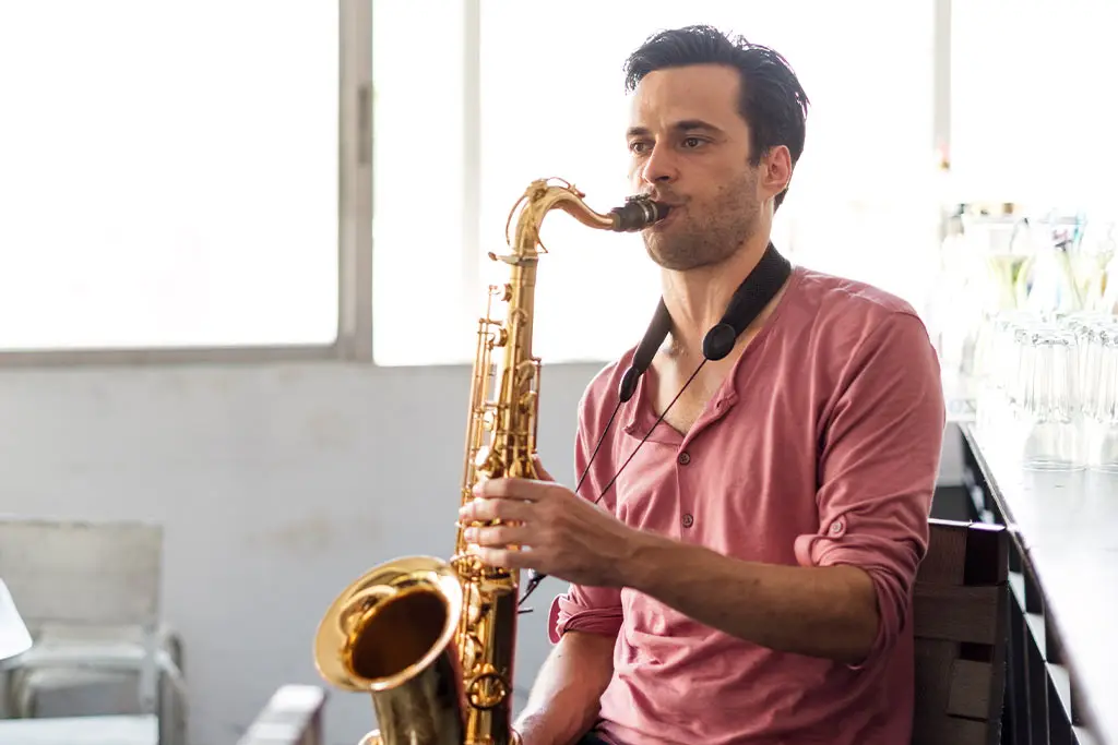 Man in a pink shirt playing tenor saxophone near glassware