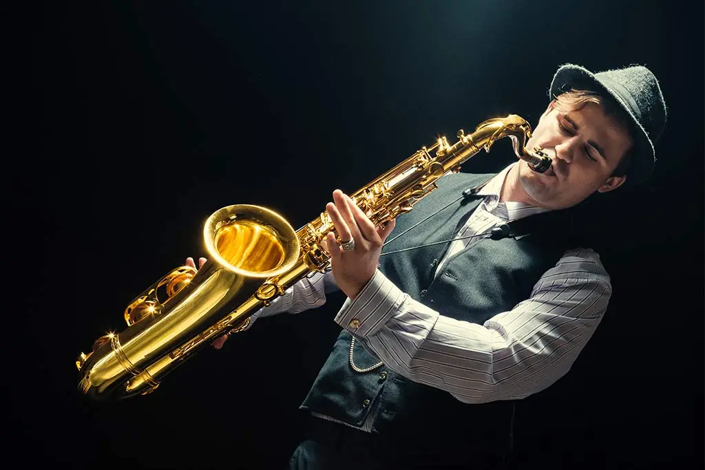 Man in a tilted hat playing tenor saxophone under a spotlight