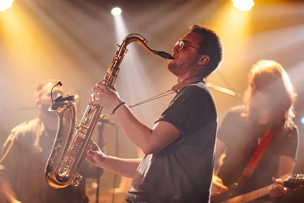 Man playing tenor saxophone on stage with band members