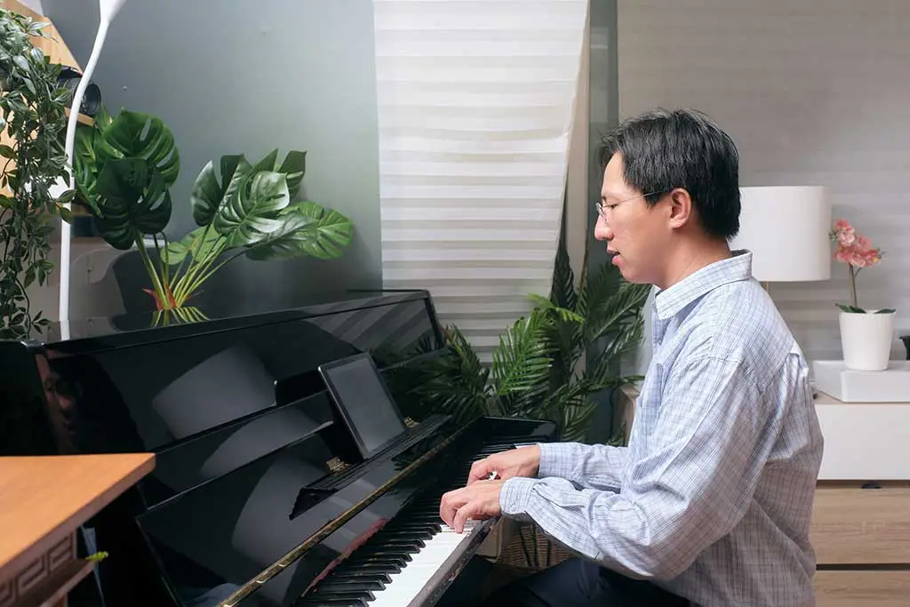 Man playing an upright piano in a room with plants
