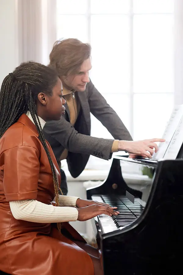 Man points to sheet music as a woman plays grand piano