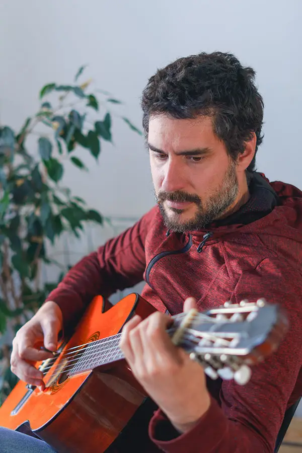 Man in a red hoodie playing a classical guitar indoors