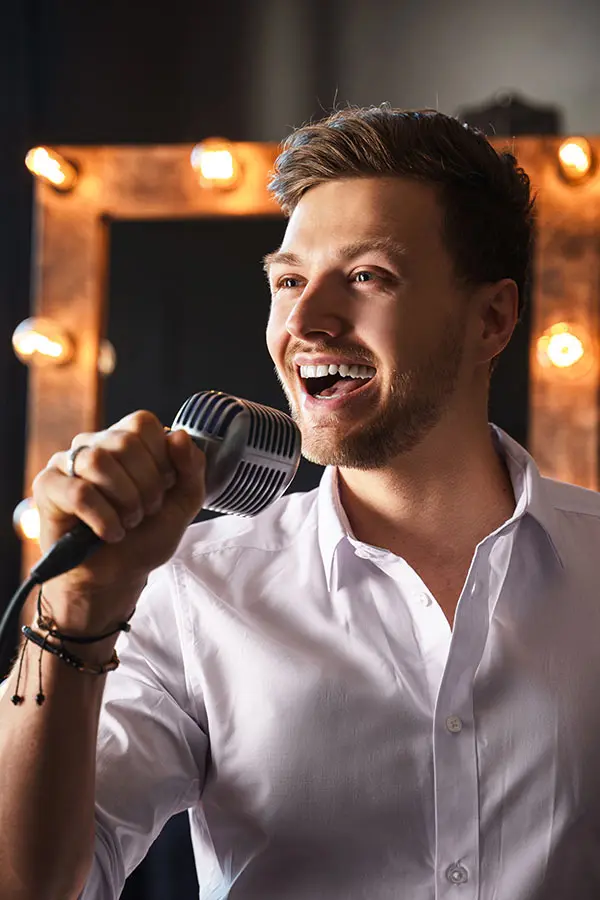 Man singing into a vintage microphone beside a lit mirror