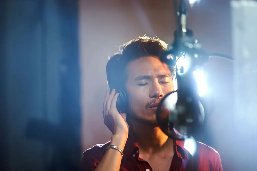 Man singing into a studio microphone while wearing headphones