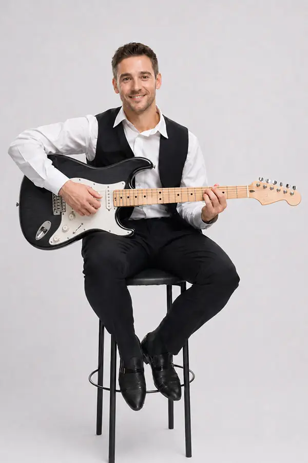 Man seated on a stool holding an electric guitar