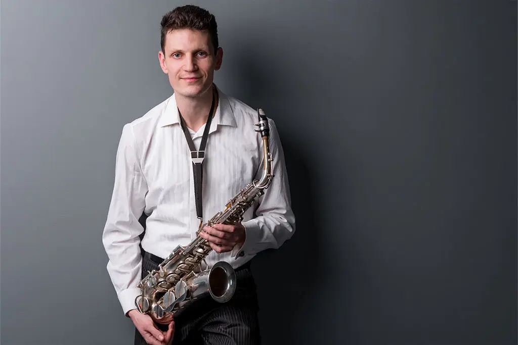Man smiling holding a saxophone