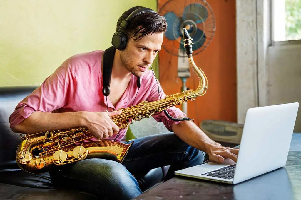 Man with tenor saxophone and headphones using a laptop on a sofa