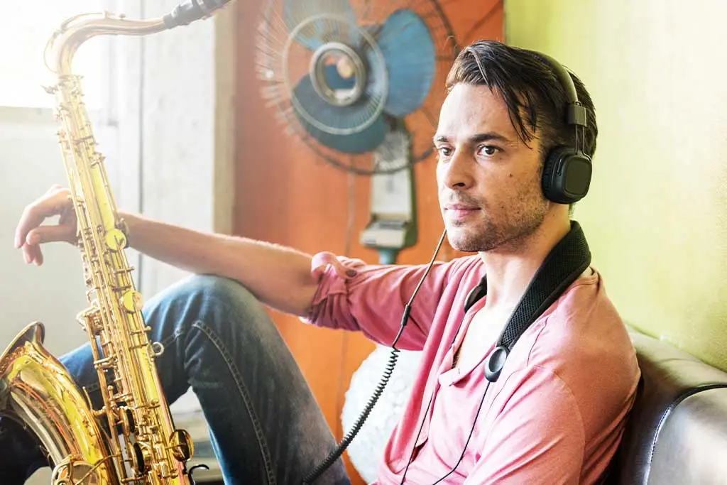 Man wearing headphones while holding a saxophone