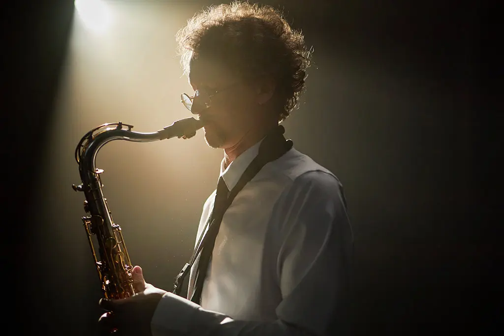 Man with glasses playing saxophone under a spotlight