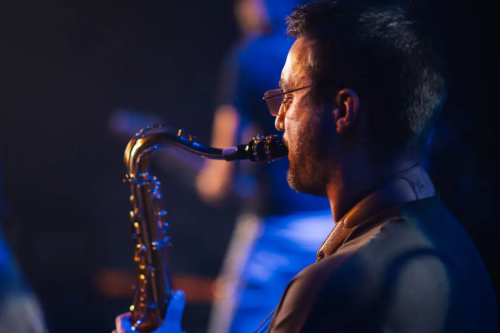 Side view of a man with glasses playing saxophone on stage