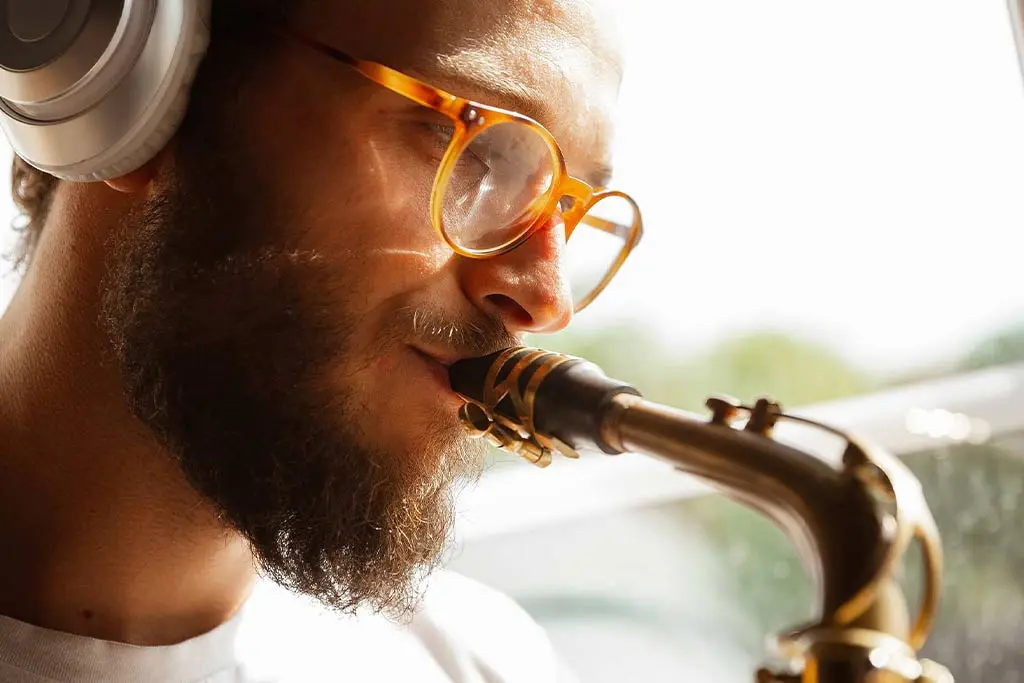 Man wearing headphones and glasses playing a saxophone