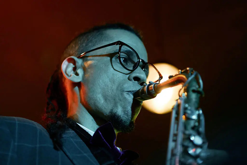 Man with round glasses playing saxophone under stage lighting