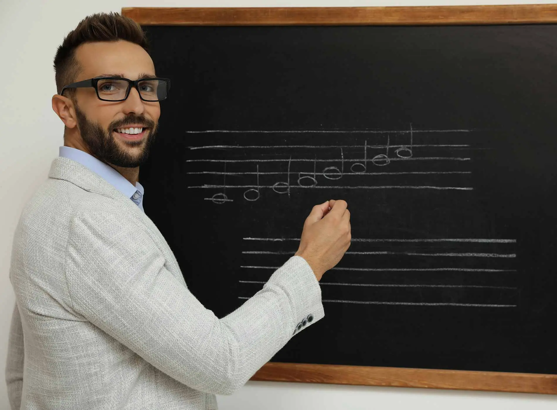 Teacher writing music notes with chalk on blackboard in classroom