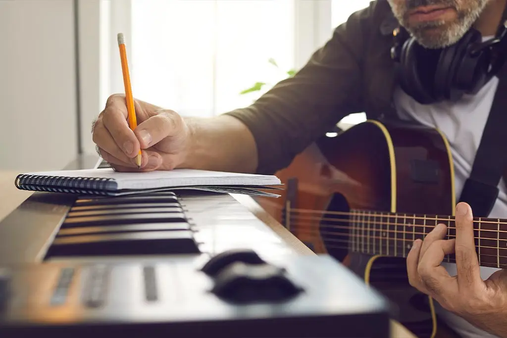 Man writing notes beside an acoustic guitar and electronic keyboard