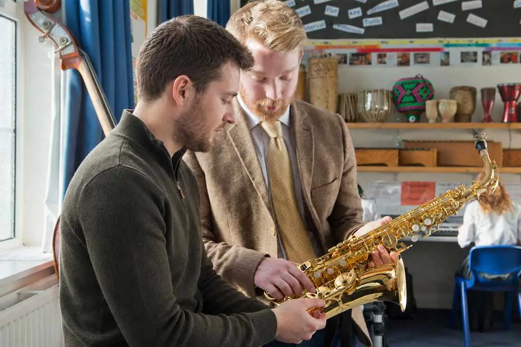 Two men examining an alto saxophone in a music classroom