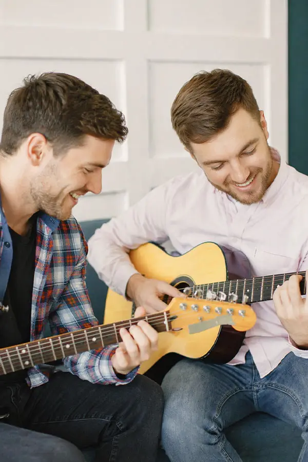 Two men smiling while playing bass guitar and acoustic guitar