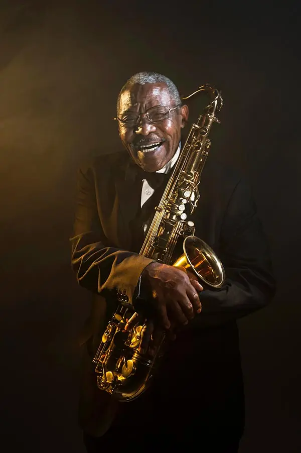 Older man smiling while holding a tenor saxophone