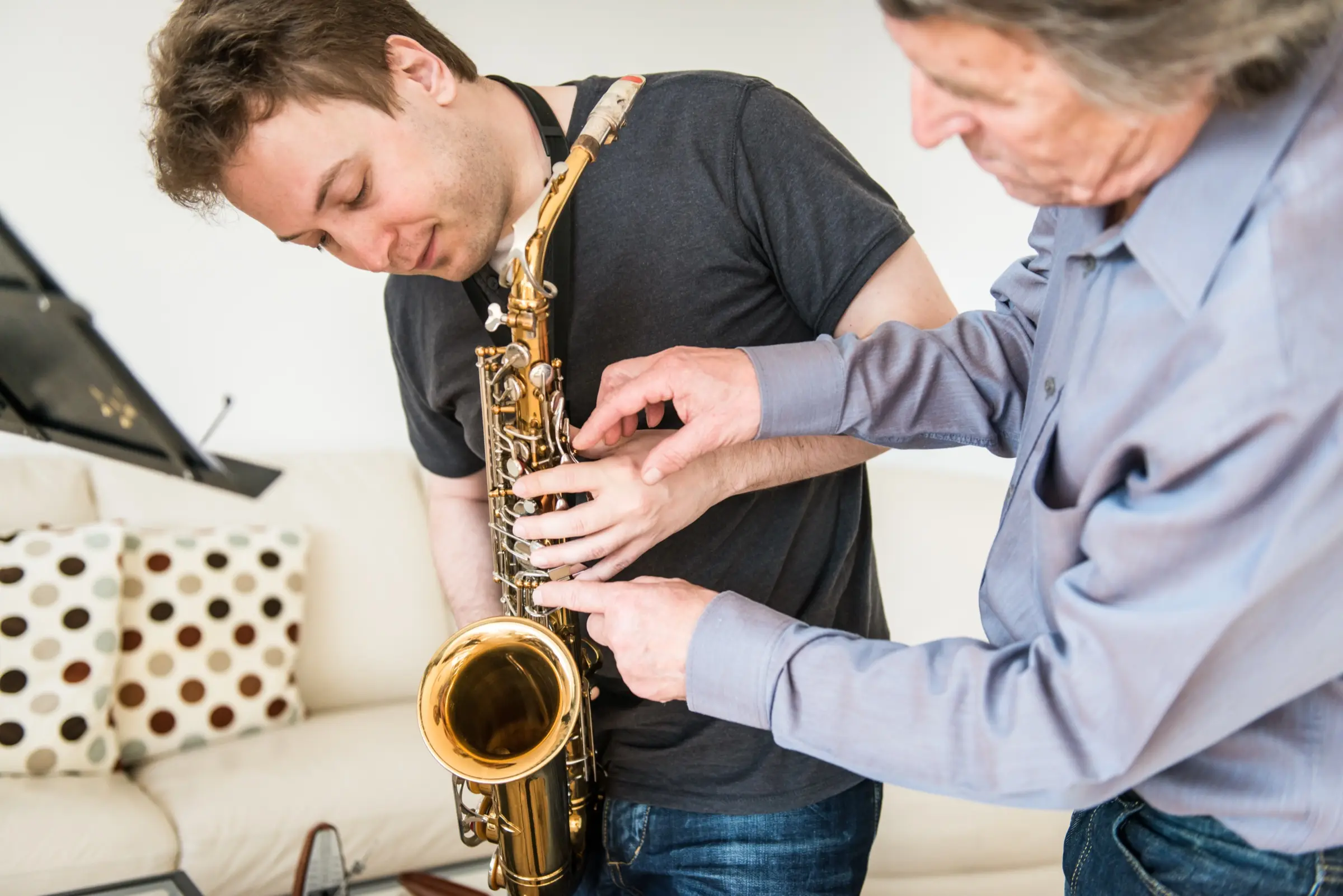 Older musician showing a young man how to hold the saxophone.