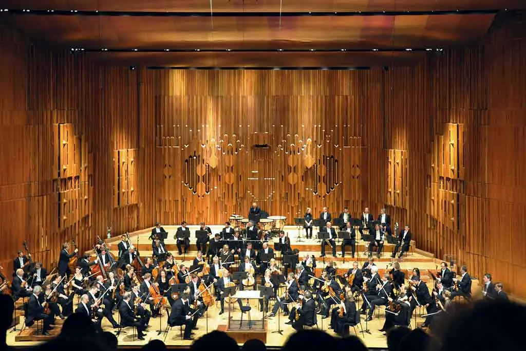 Orchestra performing on stage in a wooden concert hall
